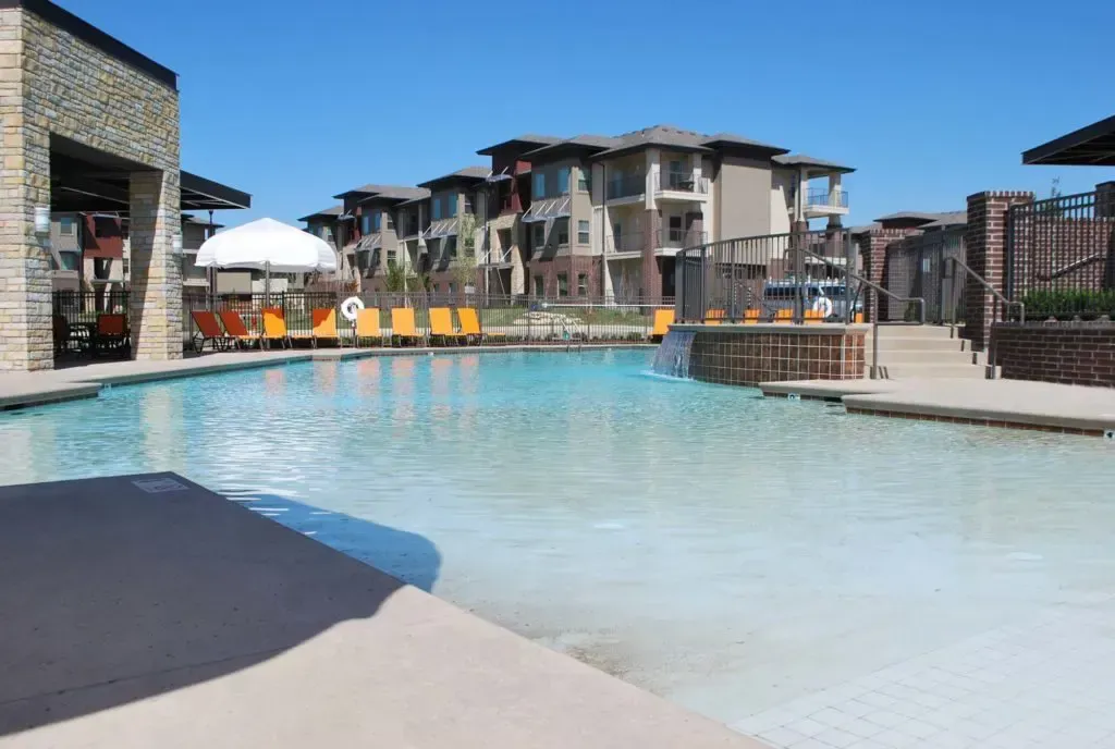 A large swimming pool surrounded by chairs and umbrellas in front of a building.