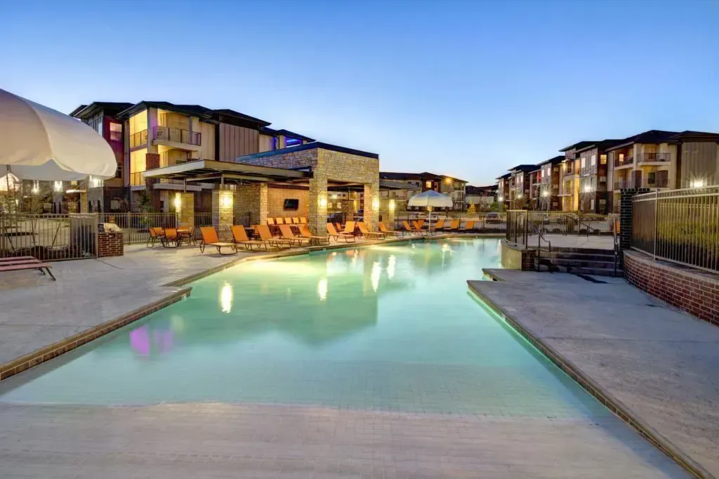 A large swimming pool surrounded by chairs and umbrellas in front of a building.
