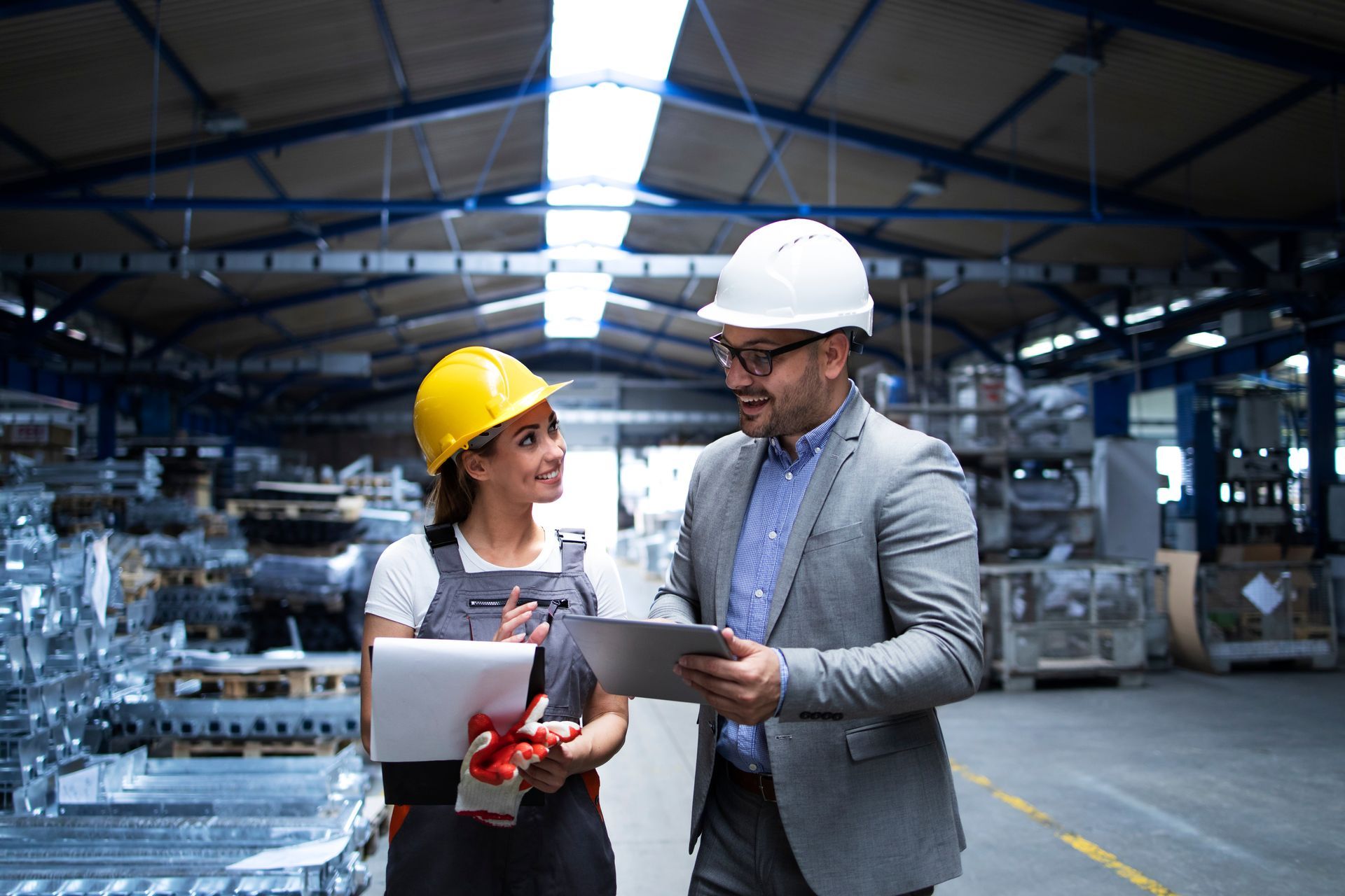 A man and a woman are looking at a tablet in a factory.