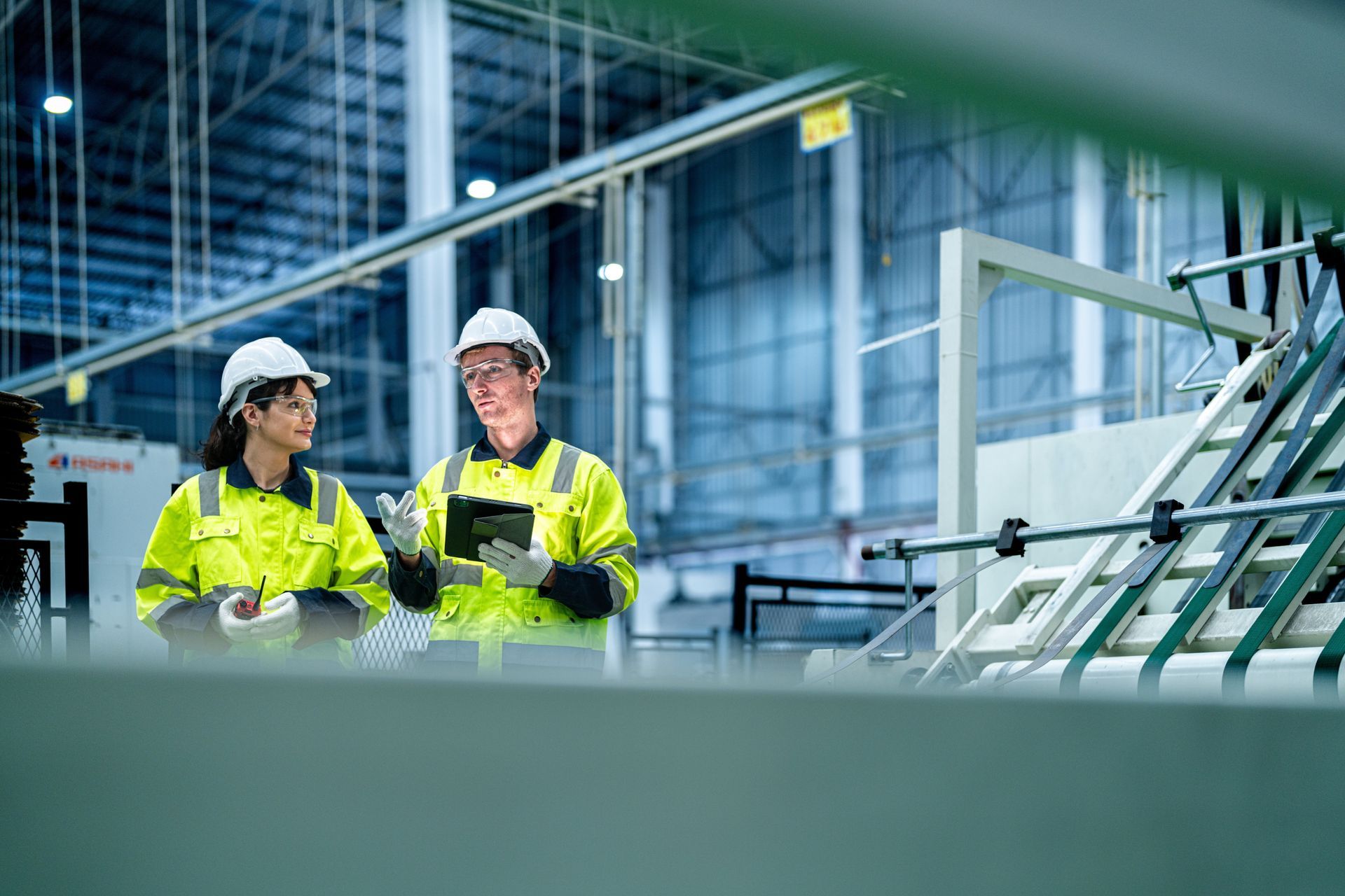 A man and a woman are standing in a factory looking at a tablet.