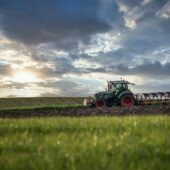 A green tractor is plowing a field of grass.