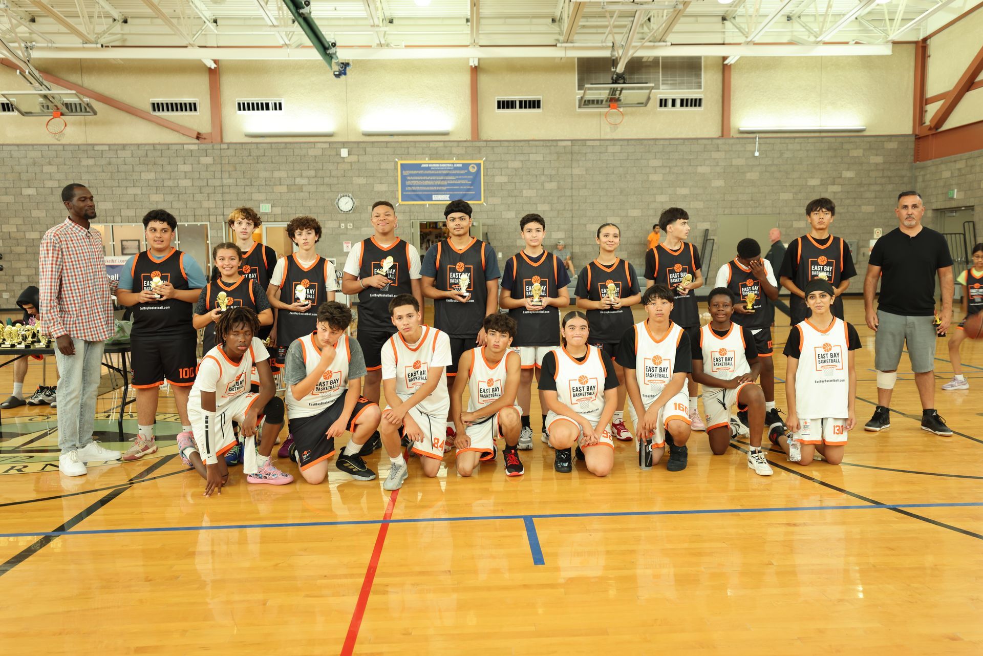 A team of basketball players and their coaches pose for a photo on an indoor wooden court.