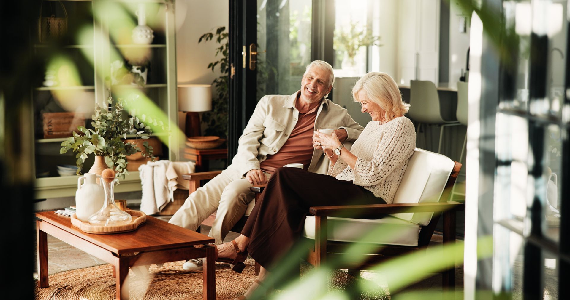 Two people sitting together on a sunlit patio, talking and reading a book at a small table