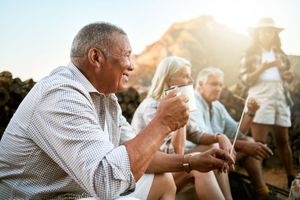 Friends sitting outdoors at sunset, sharing drinks and conversation on a campsite or patio.