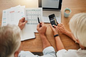 Two people reviewing bills and using a calculator at a wooden table with papers and a laptop.