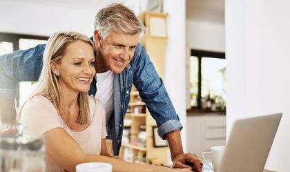 Two people smiling at a laptop in a bright home kitchen