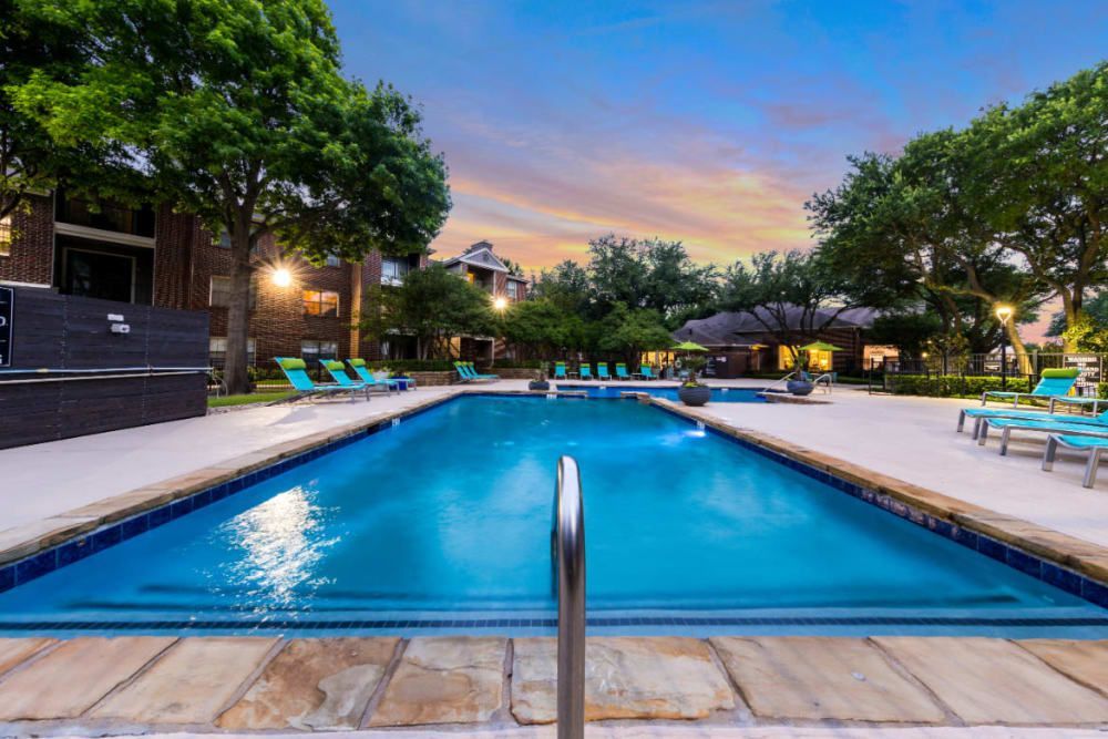A large swimming pool surrounded by chairs and trees in a residential area at Marquis at Legacy in Plano, TX.