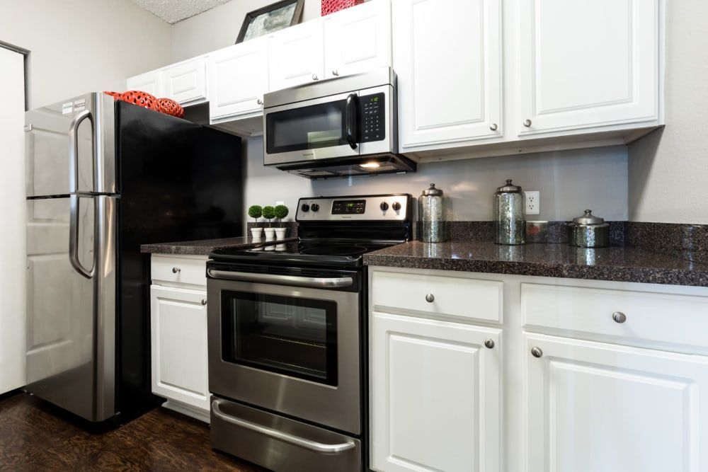 Apartment kitchen with white cabinets, stainless steel appliances, and a black refrigerator at Marquis at Legacy in Plano, TX.