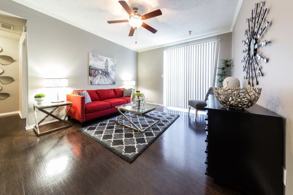 Living room with a red couch, a ceiling fan, and exit to the balcony at Marquis at Legacy in Plano, TX.