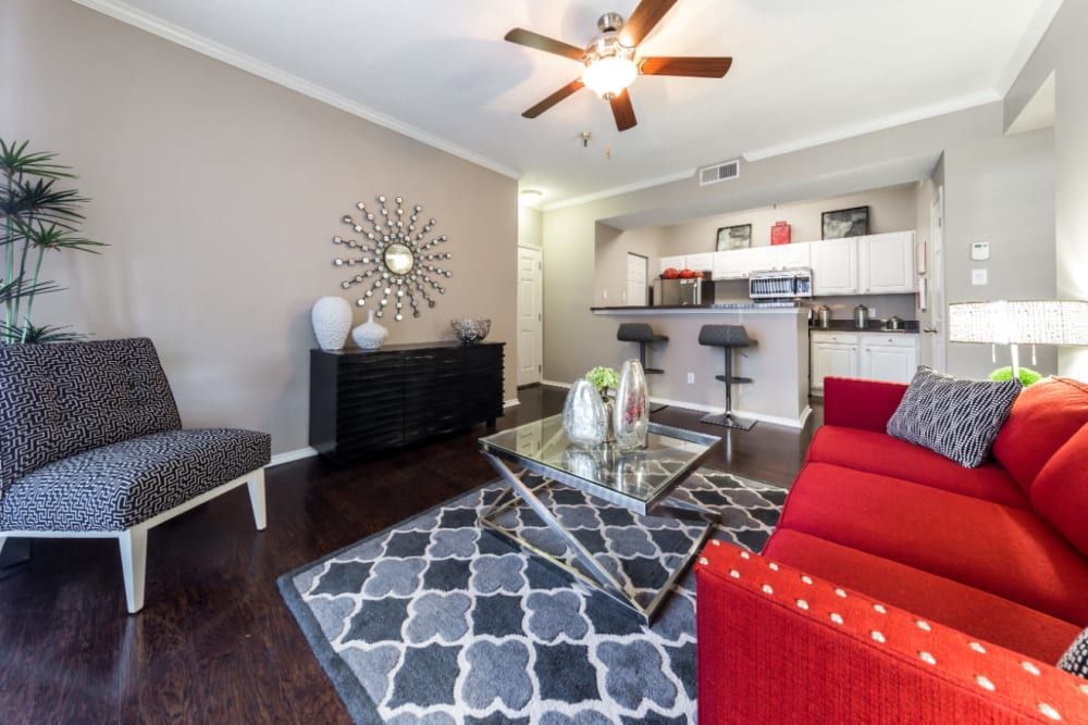 Apartment living room with a red couch, chairs, a coffee table, and a ceiling fan at Marquis at Legacy in Plano, TX.