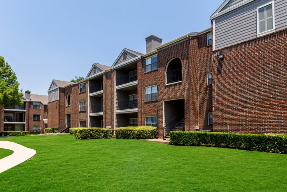 Brick apartment buildings with a lush green lawn in front of it at Marquis at Legacy in Plano, TX.