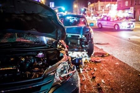 Cars damaged in a nighttime collision; police car with flashing lights in background.
