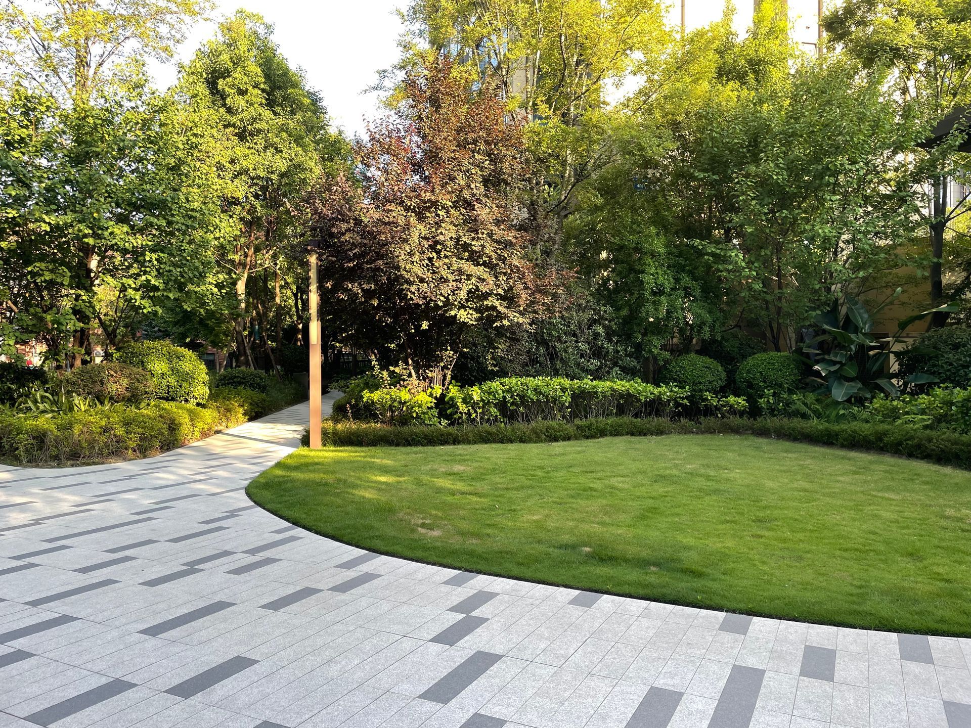 A lush green lawn curves into a patterned stone path, surrounded by trees and bushes. A lush green lawn curves into a patterned stone path, surrounded by trees and bushes.