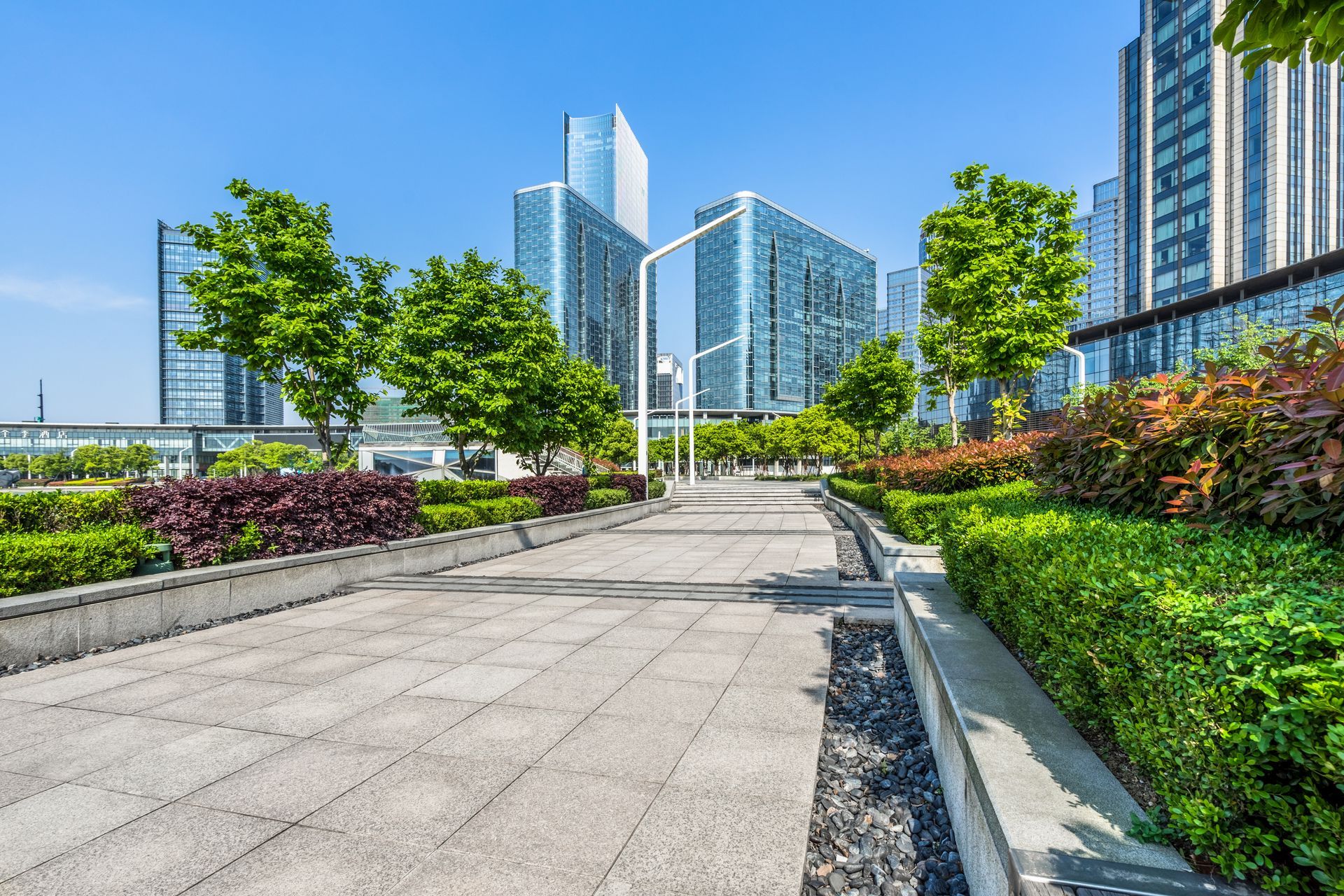 Stone pathway through green landscaping in a city park with tall glass buildings in the background. Stone pathway through green landscaping in a city park with tall glass buildings in the background.