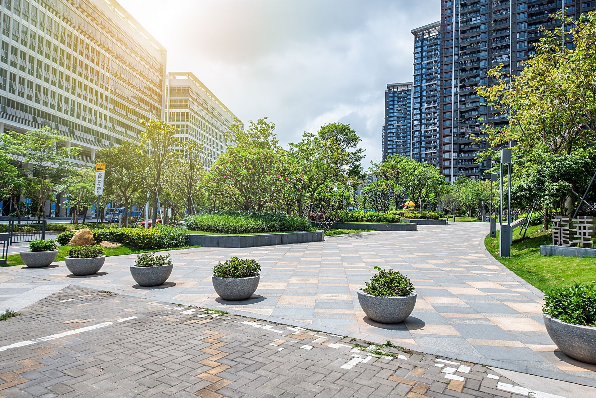Urban park with walkways, planters, trees, and tall buildings under a sunny sky. Urban park with walkways, planters, trees, and tall buildings under a sunny sky.