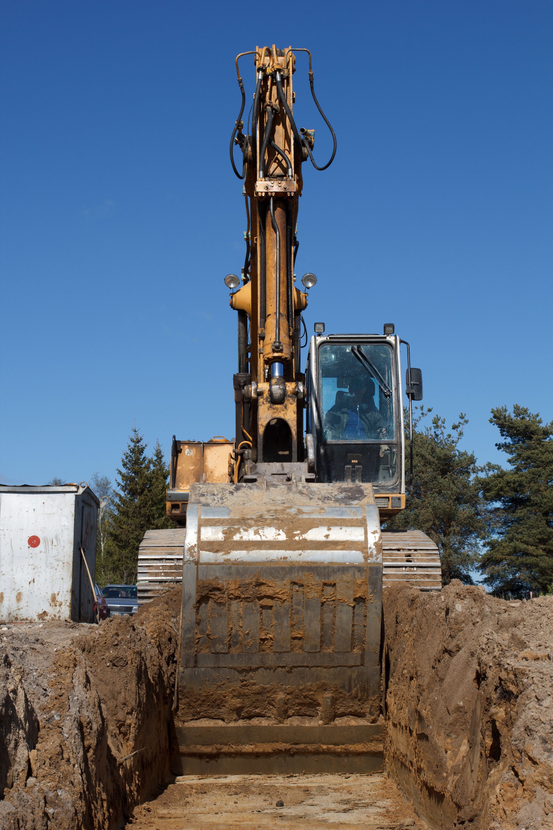 Excavator digging a trench in dirt, with blue sky background.