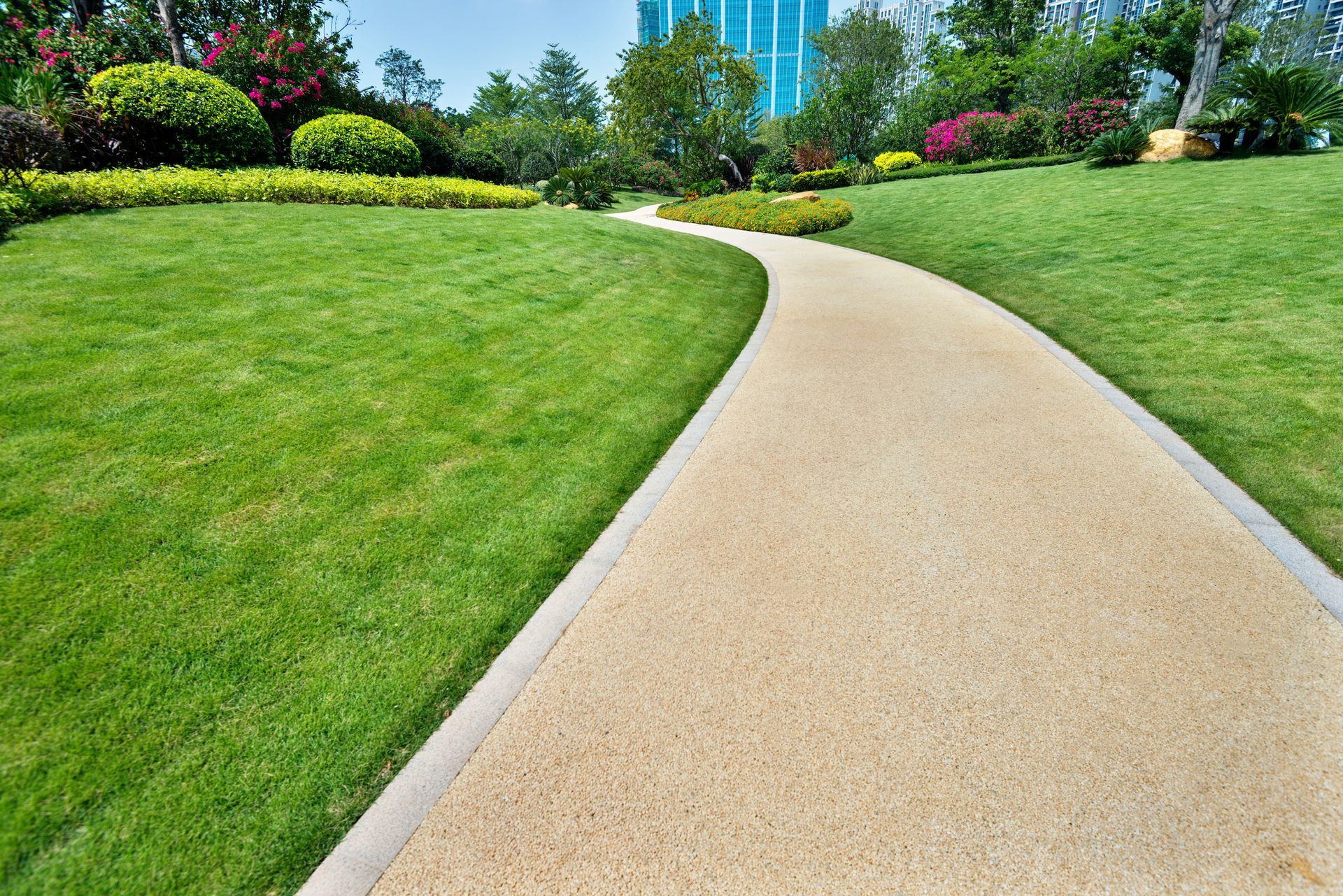Stone path curves through green lawn in a park, with trees and flowers in the background. Stone path curves through green lawn in a park, with trees and flowers in the background.