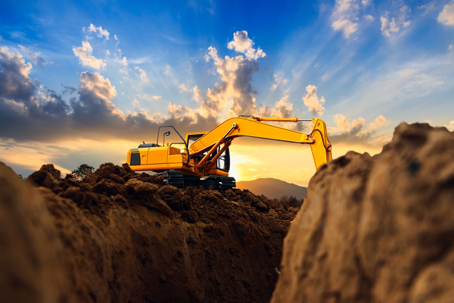 Yellow excavator digging earth against a sunset sky.