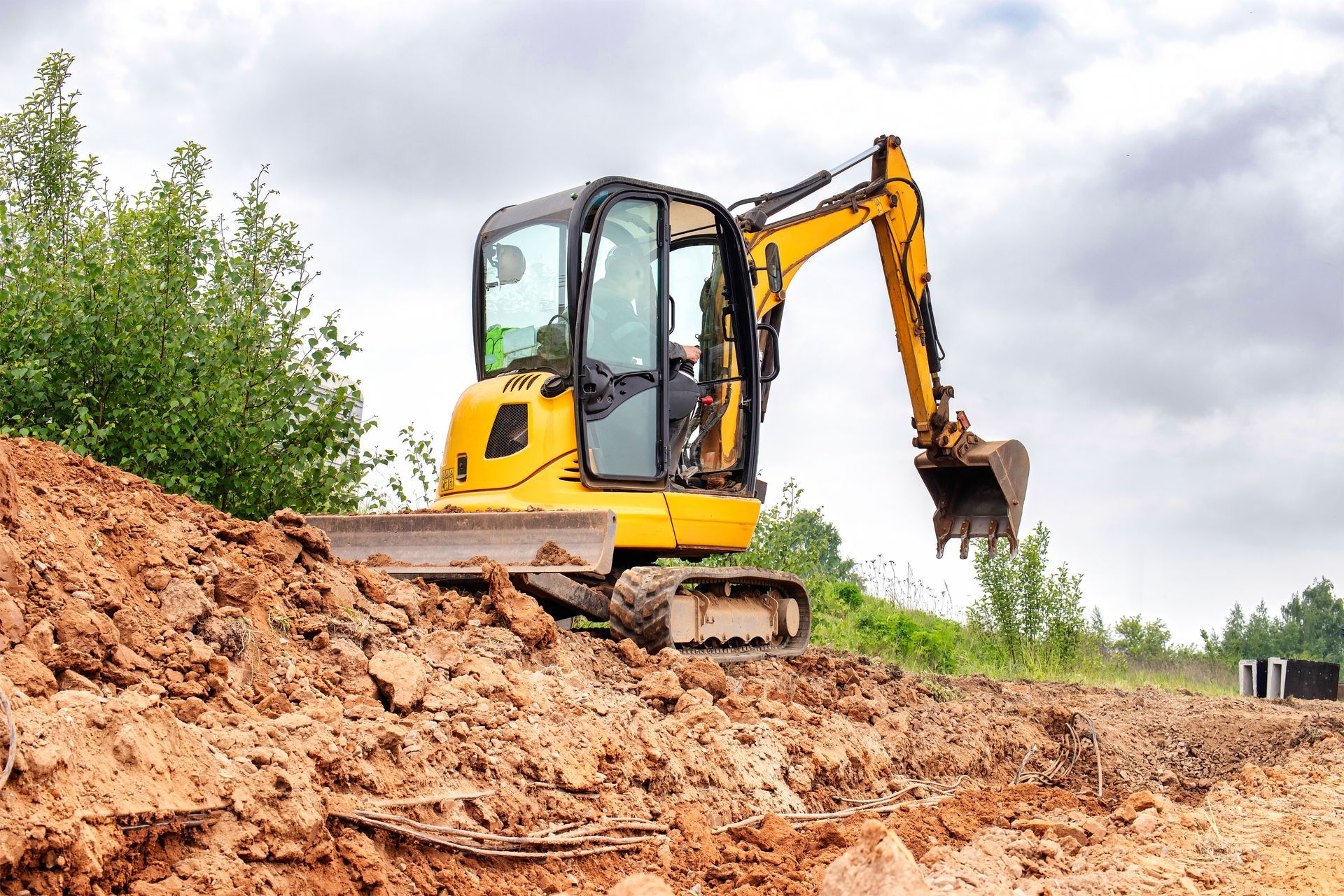 Yellow excavator digging into a mound of dirt on a construction site.