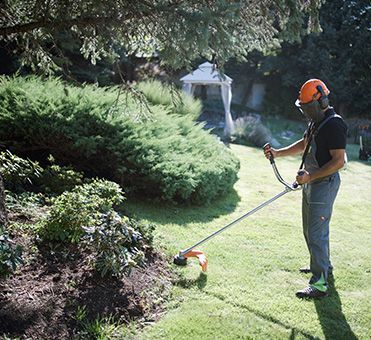 A man wearing a hard hat is cutting grass with a trimmer