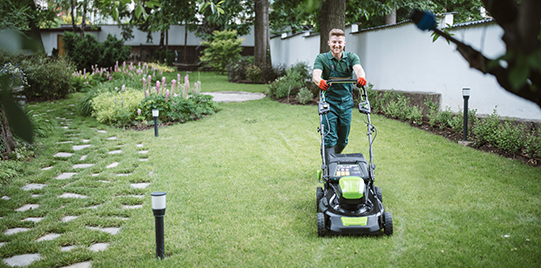 A man is mowing a lush green lawn with a lawn mower.