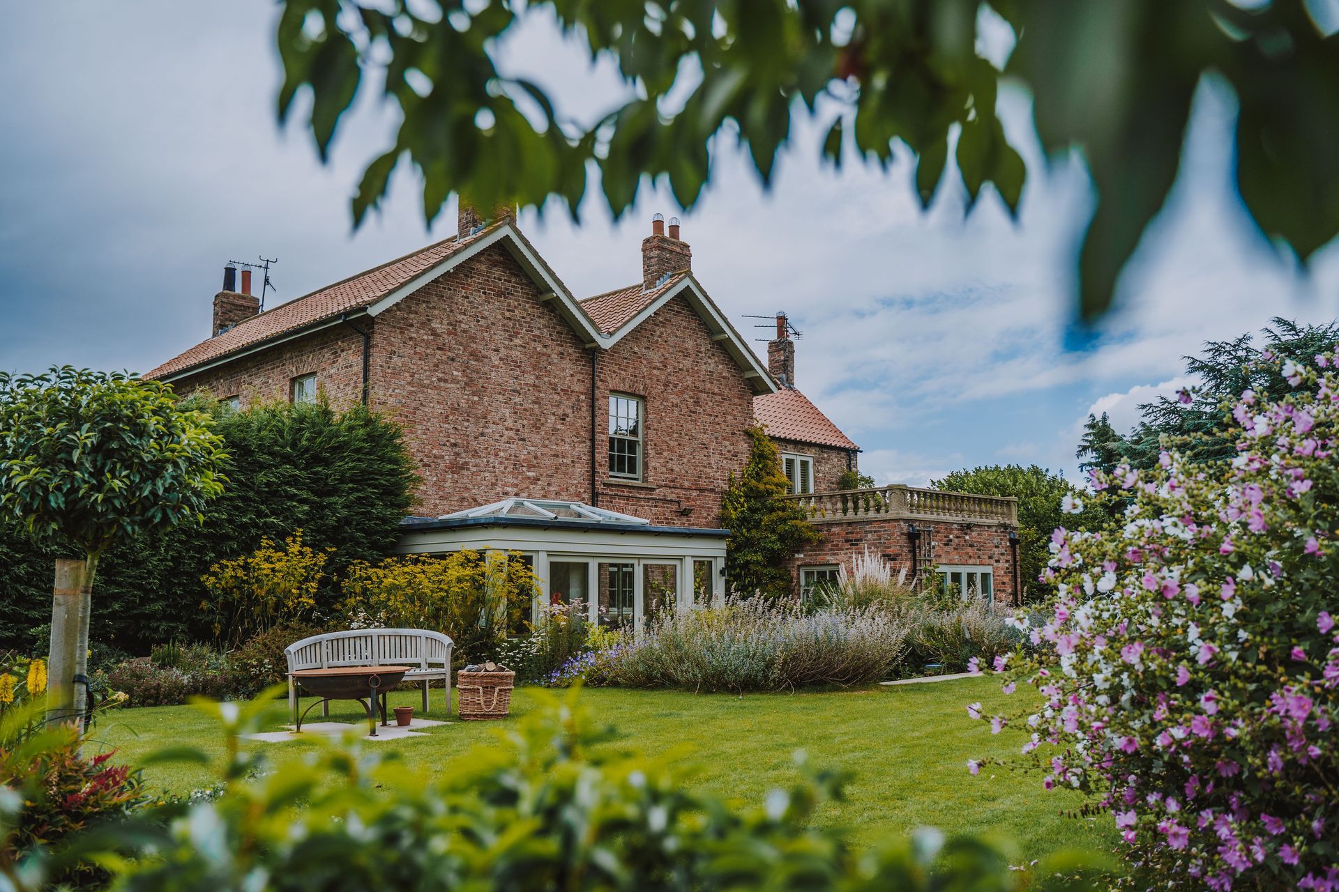 A large brick house is surrounded by a lush green garden.