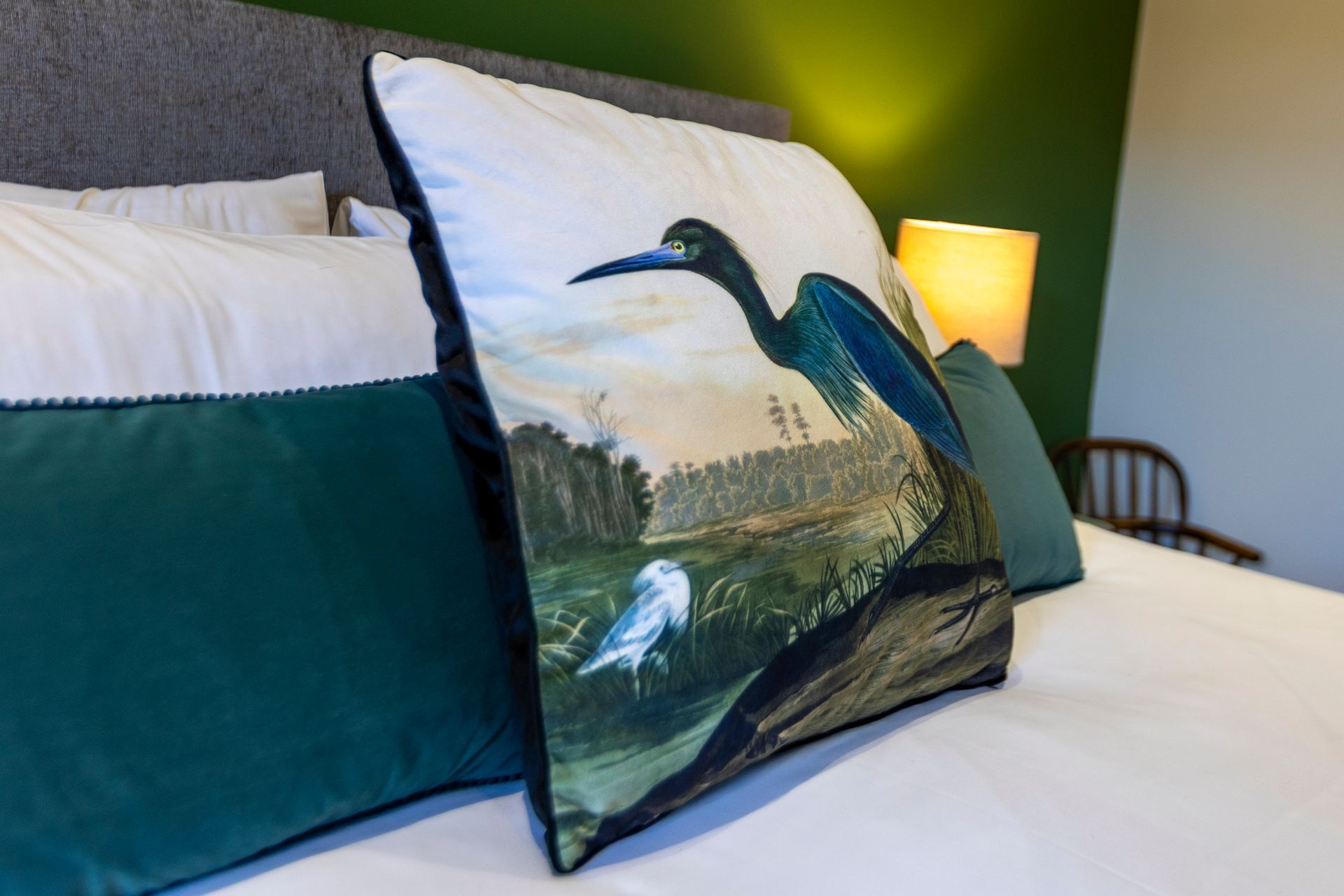 Bed with decorative pillows; the focal point is a pillow with a bird illustration.