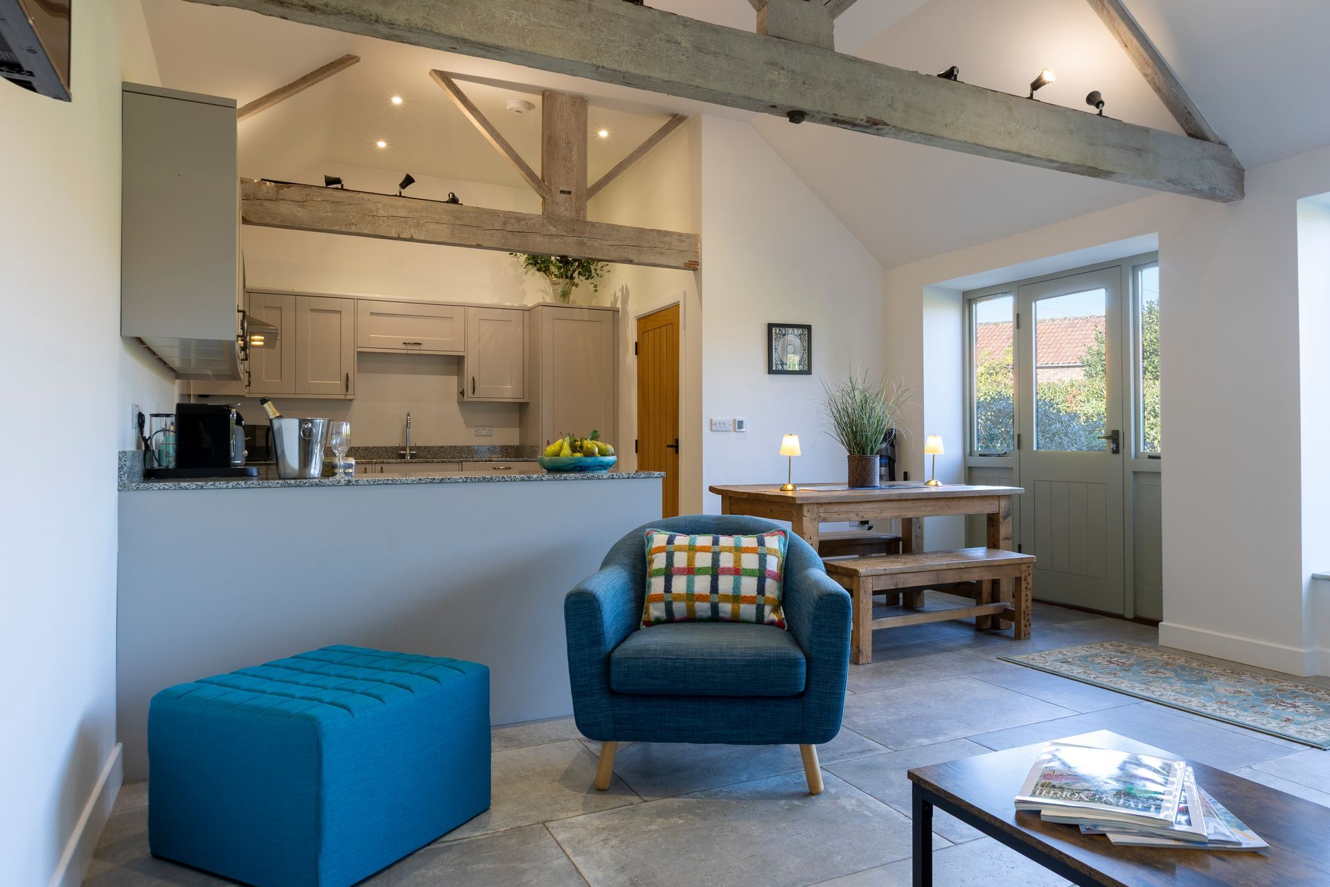 Living room and kitchen with blue furniture, wood beams, and dining area.