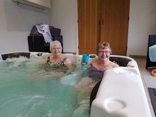 Two women are sitting in a hot tub holding wine glasses.