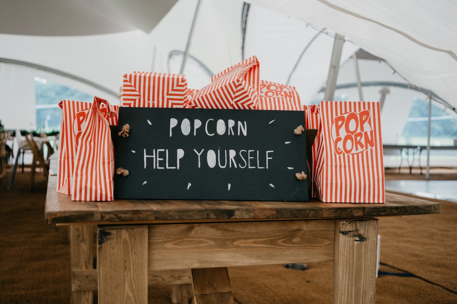 A wooden table topped with bags of popcorn and a sign that says `` popcorn help yourself ''.