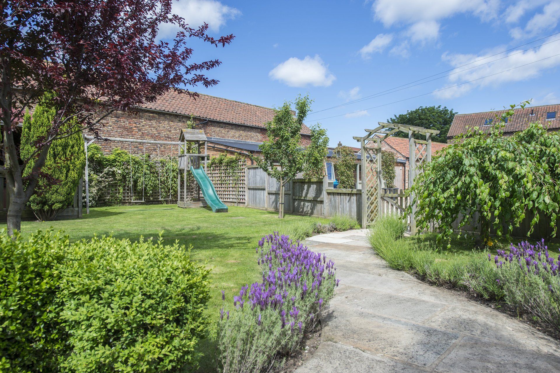 A path leading to a playground in a garden with purple flowers.