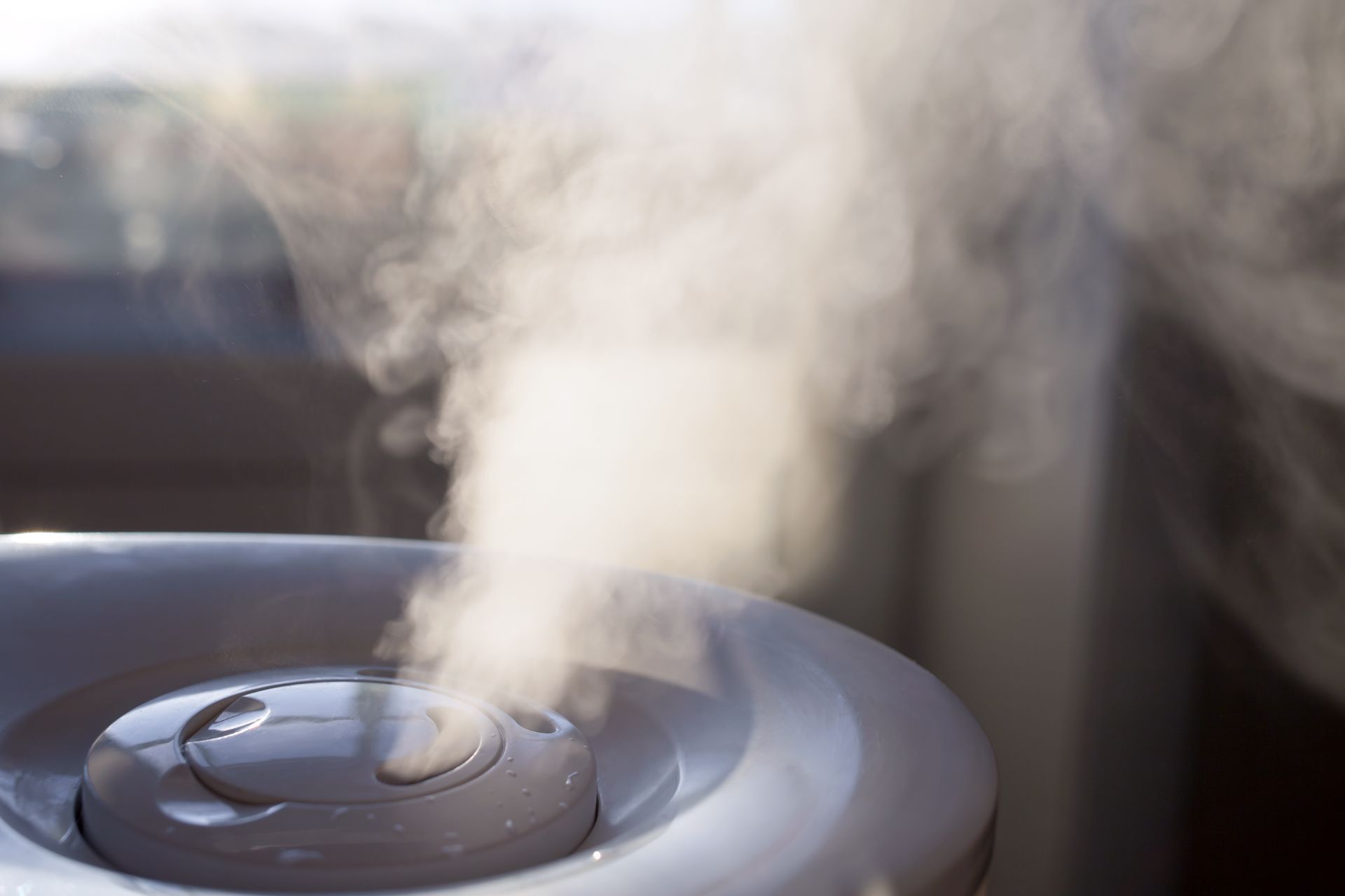 Un humidificateur diffusant de la vapeur blanche dans l'air, avec un panneau de commande gris.
