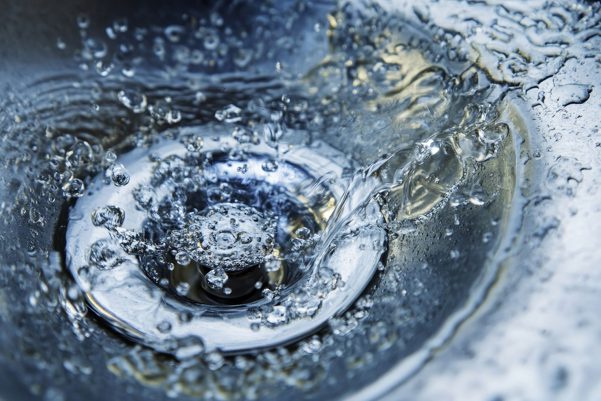 Un serpentin de plomberie métallique flexible est inséré dans la canalisation d'un évier en acier inoxydable.