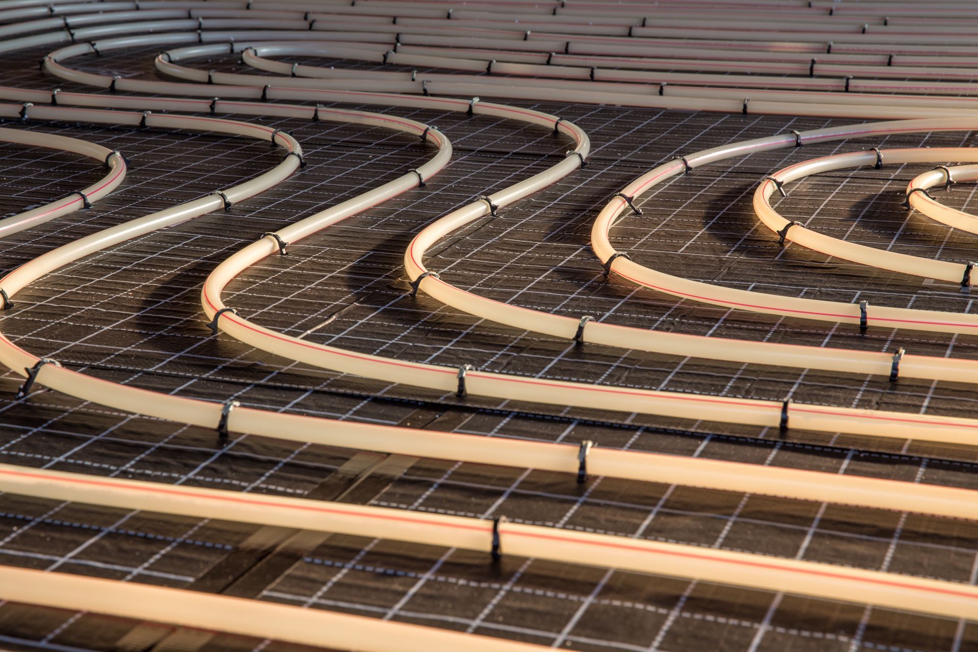 Tuyaux de chauffage au sol rayonnant enroulés sur une grille foncée, prêts à être installés.