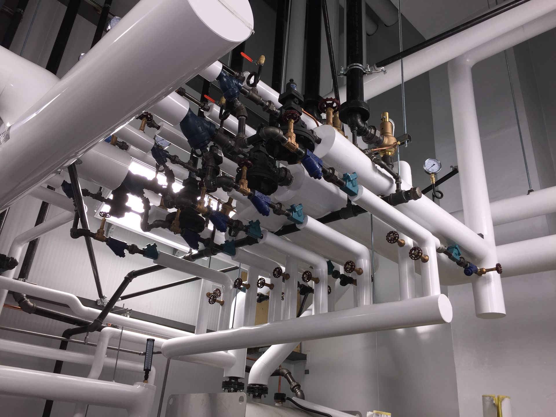 Tuyaux et vannes isolés blancs dans un environnement industriel, avec manomètres et raccords visibles.