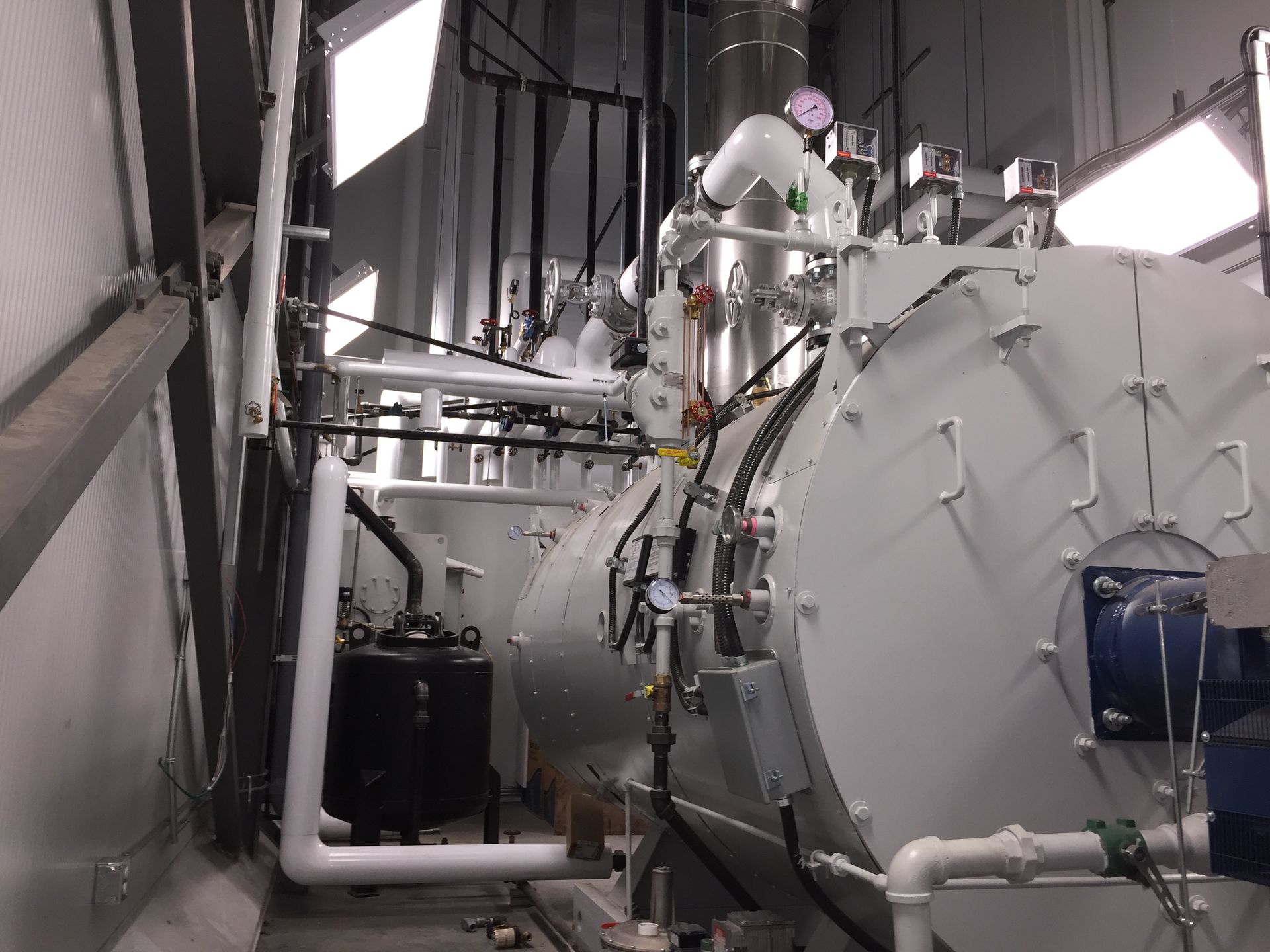 Chaudière industrielle blanche avec tuyaux et manomètres dans une pièce blanche.