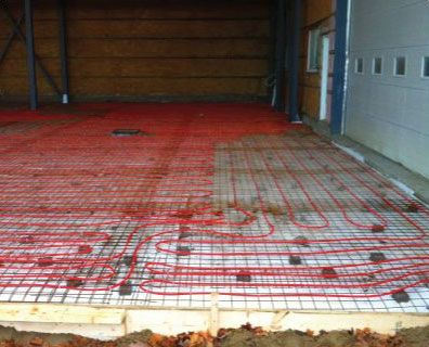 Tubes de chauffage au sol radiant rouges posés sur un treillis métallique, prêts pour le coulage du béton à l'intérieur d'un bâtiment.