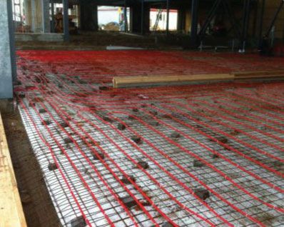 Des câbles chauffants rouges sont installés sur une grille, prête pour le coulage du béton dans un bâtiment en construction.