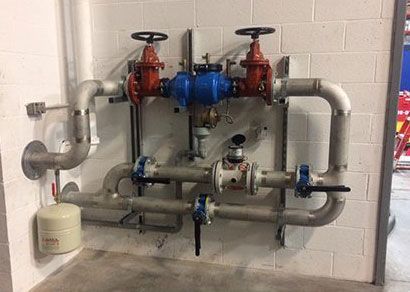 Tuyaux d'eau et vannes sur un mur de briques blanches ; les vannes sont rouges, bleues et blanches.