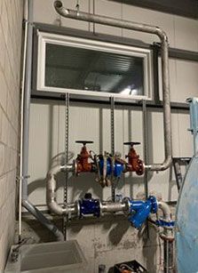 Système de plomberie avec tuyaux, vannes et fenêtre. Vannes rouges et bleues, tuyaux en acier inoxydable et fenêtre à cadre blanc.