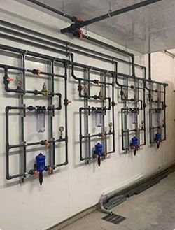 Tuyaux et vannes installés sur un mur, probablement pour la filtration de l'eau, dans un contexte utilitaire ou industriel.