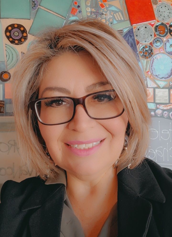 A woman wearing glasses and a black jacket is smiling for the camera.