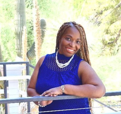 A woman in a blue tank top is leaning on a railing and smiling.