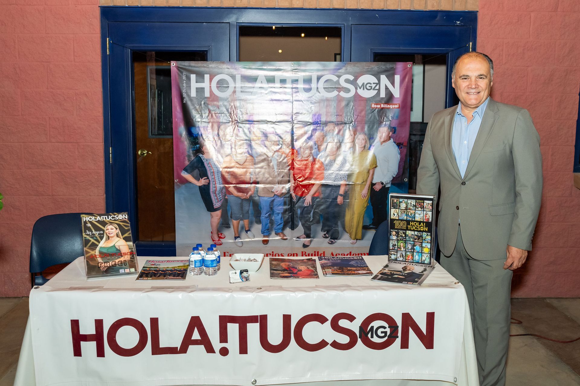 A man in a suit is standing in front of a table that says hola tucson