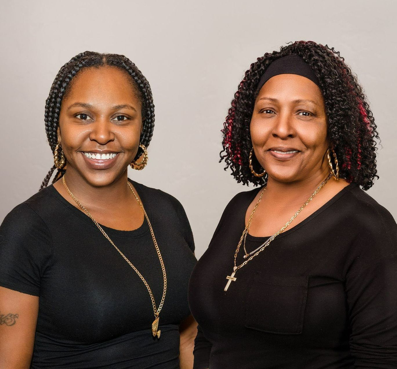 Two women standing next to each other wearing black shirts and gold necklaces