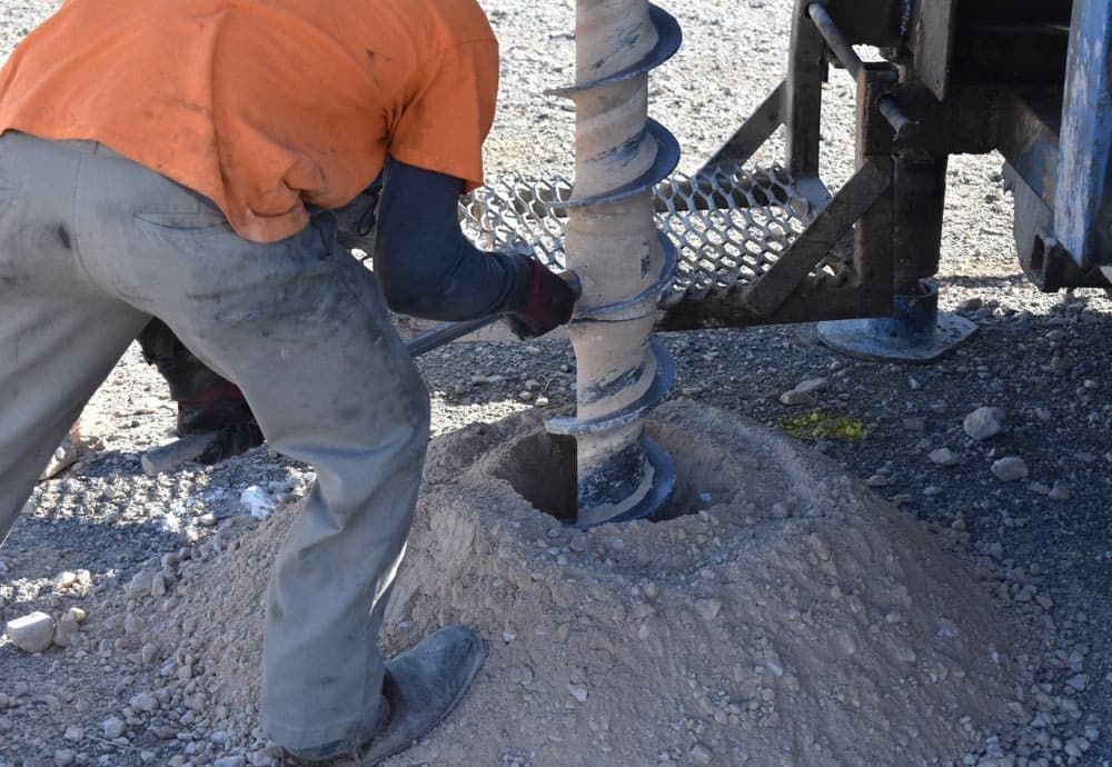 A Man Is Using A Drill To Dig A Hole In The Ground — TJ’s Bobcat Excavator Hire In Woodburn, NSW
