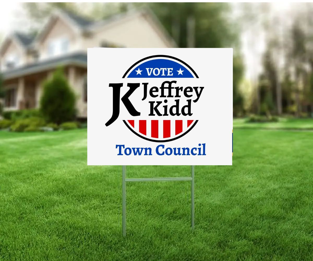 Yard sign for Jeffrey Kidd for Town Council. White sign with blue, red, and black logo in front of a house.