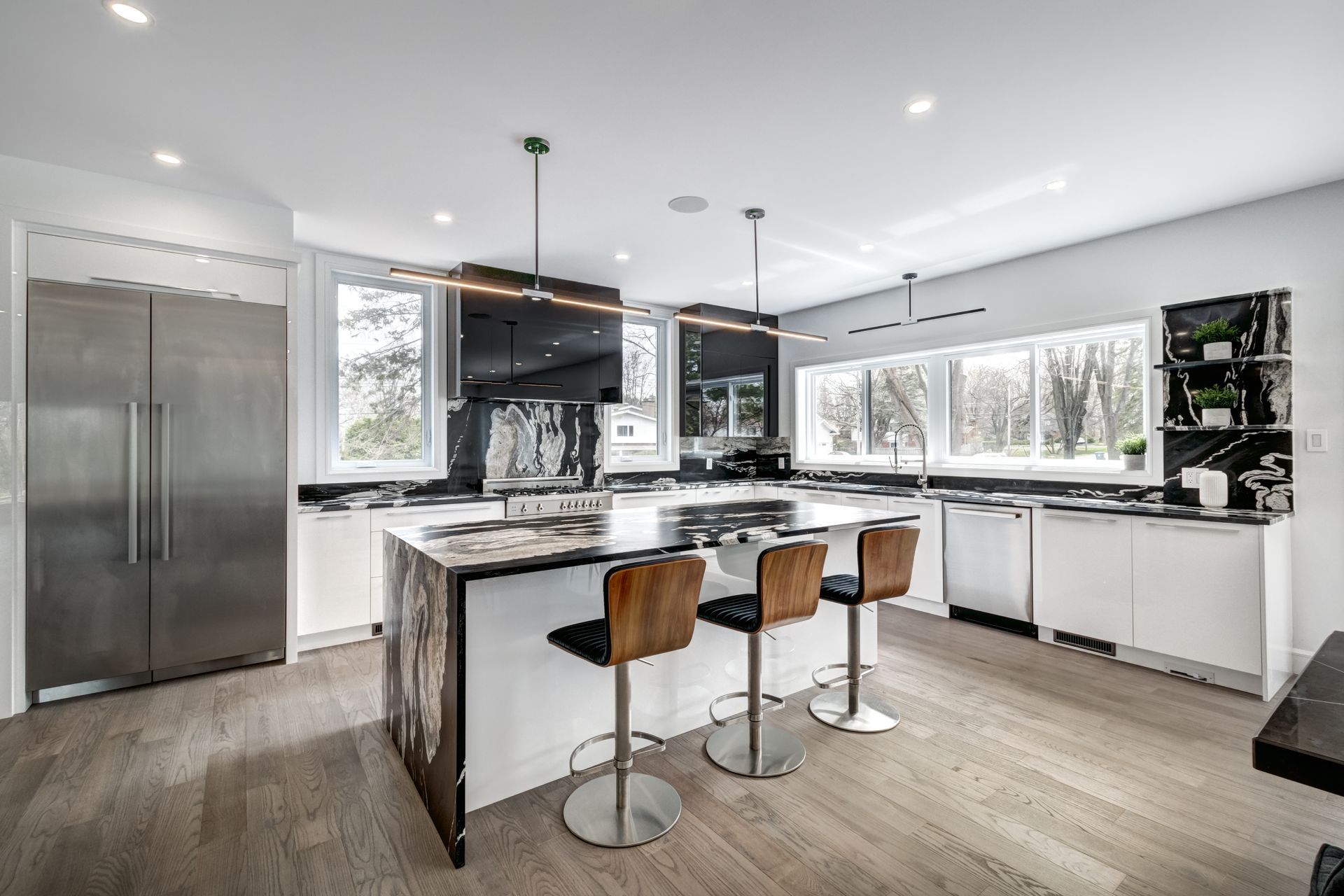 Modern kitchen with stainless steel appliances, white cabinets, island with stools, and large windows.