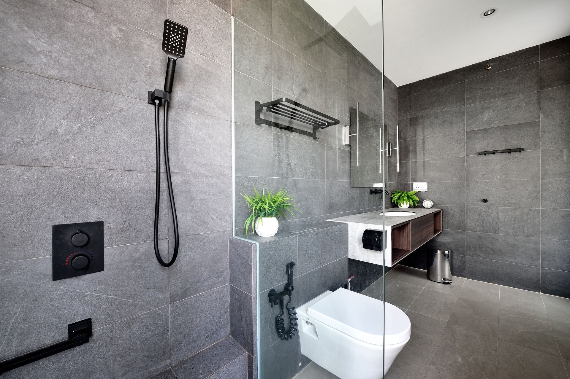 Modern bathroom with gray stone walls, black fixtures, and a glass shower.