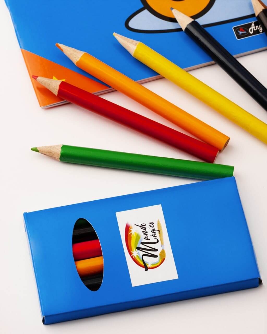 Una caja de lápices de colores se encuentra al lado de un libro.